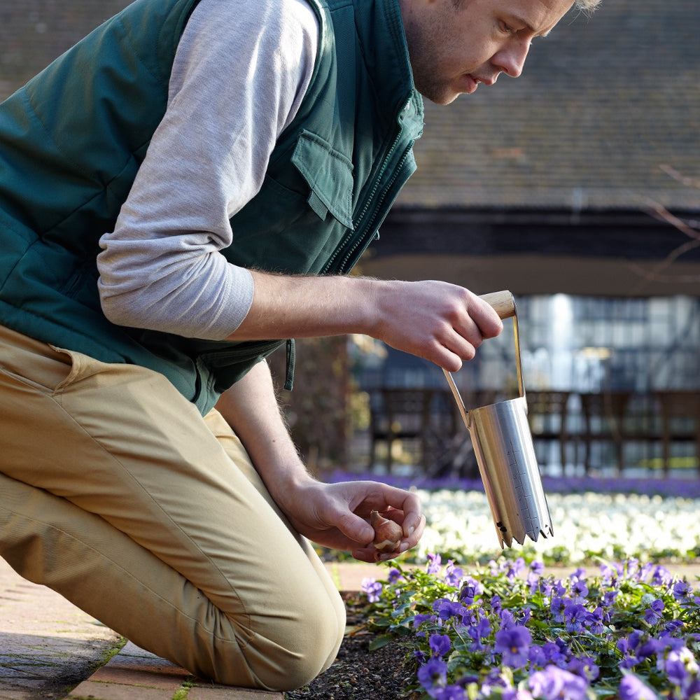 man kneeling in garden using bulb planter gardening tool