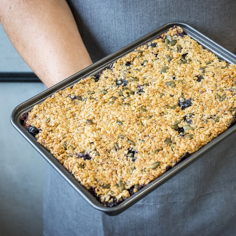 man wearing apron holding baking tin of flapjack