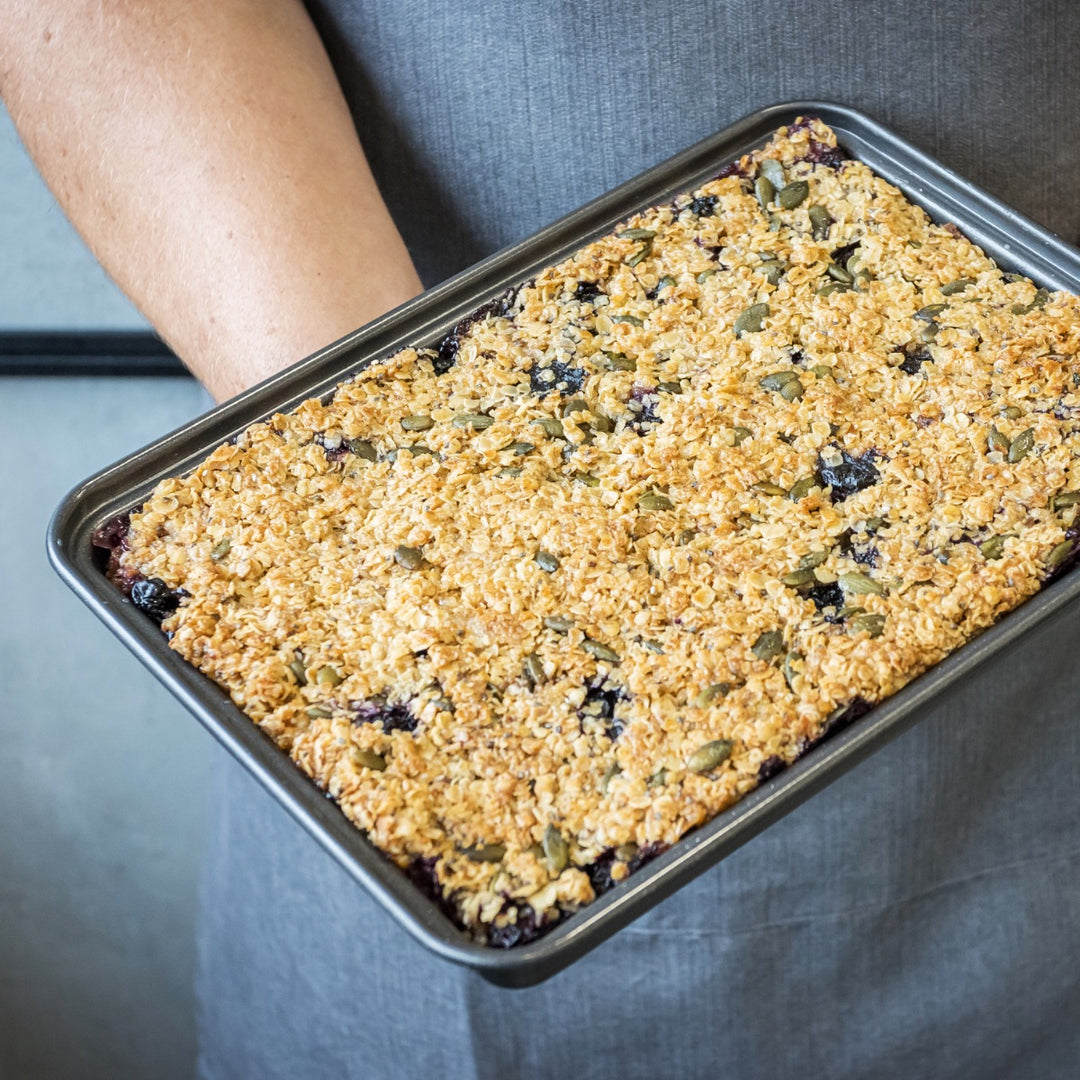 man wearing apron holding baking tin of flapjack