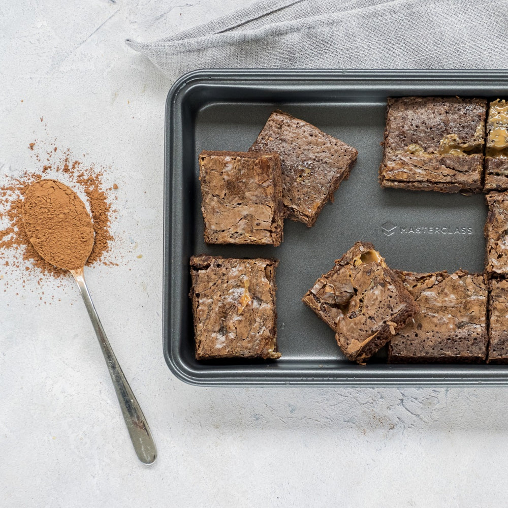 cake tin with slices of brownies on tabletop with spoon of cocoa